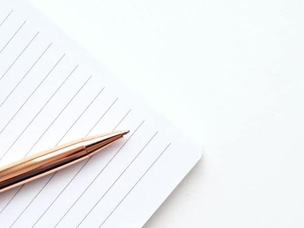 A close-up shot of a gold pen on a lined notepad with a white background, offering ample copyspace.